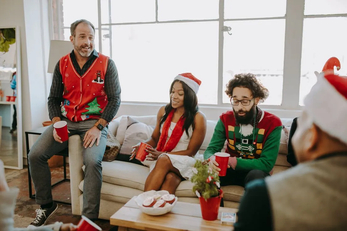 Coworkers in holiday sweaters and Santa hats chatting at a festive office party