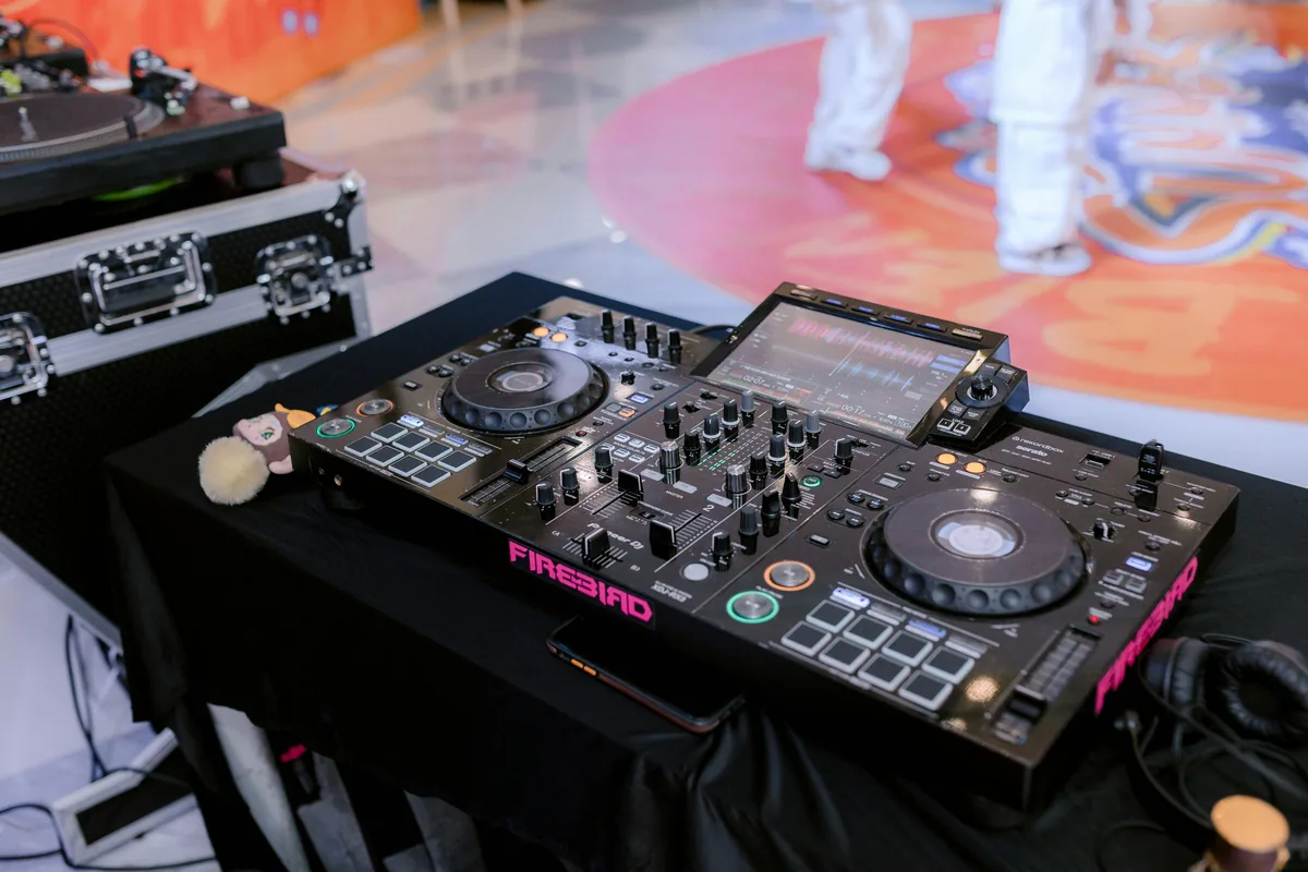 Pioneer Firebird DJ controller set up at a professional event, with performers visible on a colorful dance floor in the background