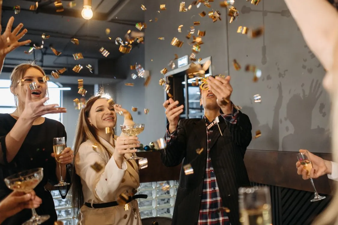 Friends toasting with champagne as gold confetti falls at a New Year's Eve party