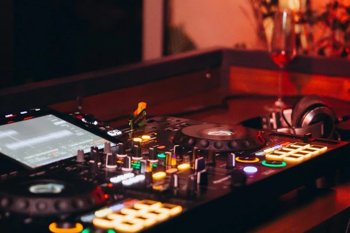 Close-up of a Pioneer DJ controller with colorful LED lights glowing at an upscale event, with a wine glass in the background