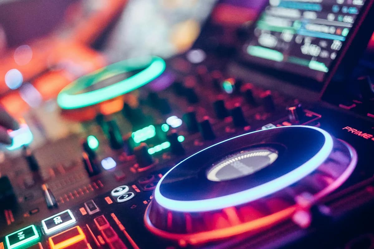 Denon Prime DJ controller glowing with teal and red LED lights at an upscale event with warm purple ambient lighting